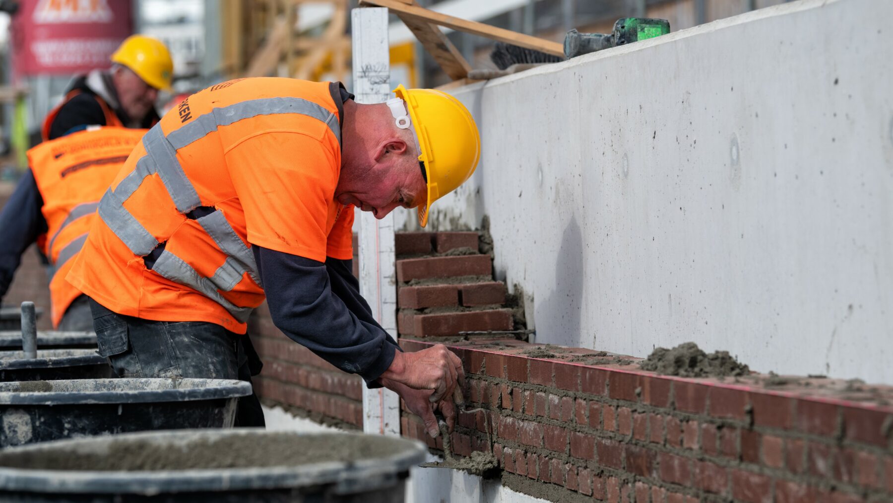 Metselaar metselt een bakstenen kademuur tegen een betonnen L-wand