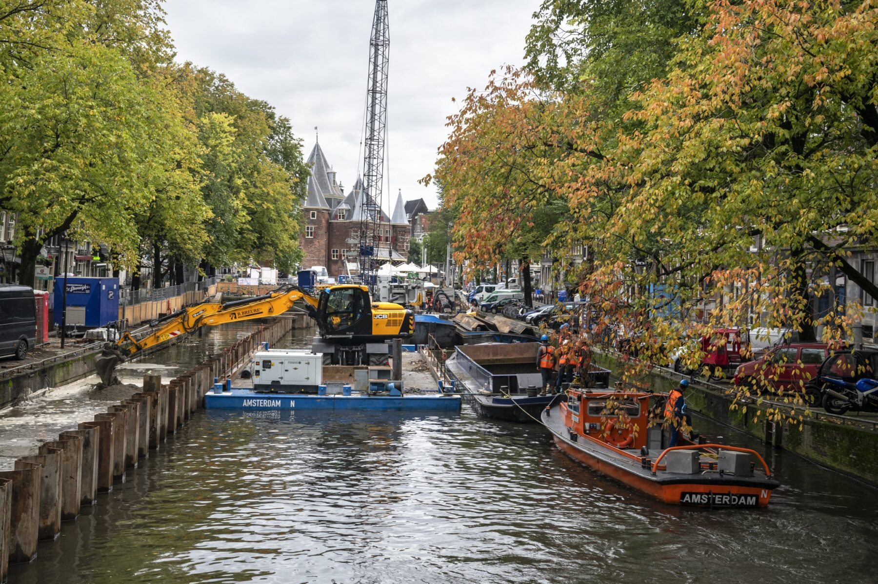 Een graafmachine stort zand tussen damwanden en de kade aan de Kloveniersburgwal